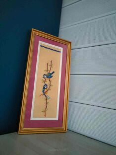 Obrazek z sikorkami wyszywany oparty pod kątem o róg między sidingiem a granatową ścianą