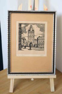 Przepiękna litografia Prašná brána w czarnej ramce na tle ściany


