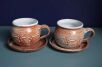 Ceramiczne kubki beczułki ze spodkami z uszkami odwróconymi po drugiej stronie