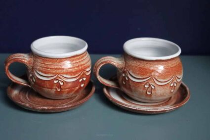 Ceramiczne kubki beczułki ze spodkami z uszkami po lewej na granatowym tle