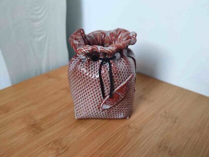 Pojemnik w kształcie sakiewki na długopisy na drewnianej powierzchni i na tle białej ściany