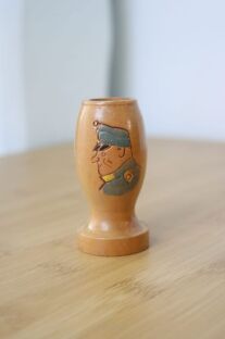 Stary drewniany świecznik ze Szwejkiem z widocznym jego wizerunkiem w mundurze i na jasnym rozmazanym tle