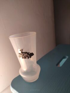 Wazonik mleczny na niebieskim krzesełku z widocznym cynowym wizerunkiem jelonka z bliska