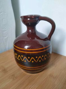 Brązowy dzbanek ceramiczny na drewnianej powierzchni z wyraźnymi jasnymi wzorami