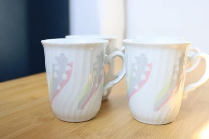 4 kubki  z wzorem konwalii Dux Porcelán ułożone po dwa obok siebie na drewnianej powierzchni