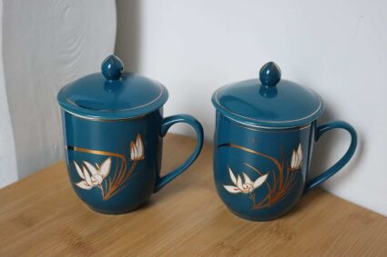 Dwa kubki z przykrywką bliskie turkusu do zaparzania z elementami kwiatów na tle ściany