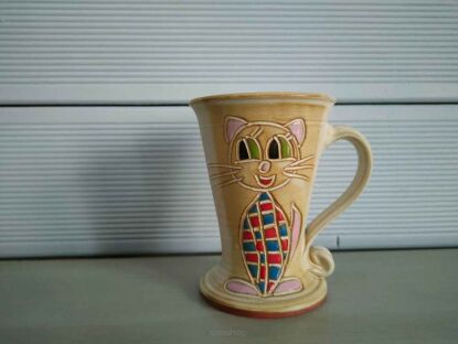 Ceramiczny kubek z wyraźnym wizerunkiem kotka  stojący tuż przed jasnym sidingiem