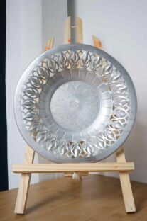 Piękny metalowy talerz produkcji radzieckiej na drewnianej sztaludze i białej powierzchni