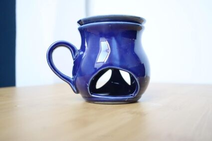 Kominek granatowy z wolnym miejscem na olejki na drewnianej powierzchni z uszkiem z lewej strony
