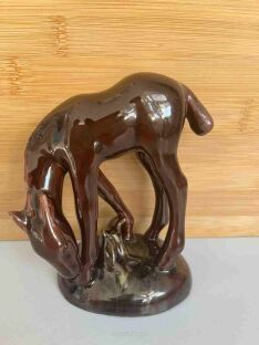Brązowa figurka konika ceramicznana na podstawce jedzącego trawę
